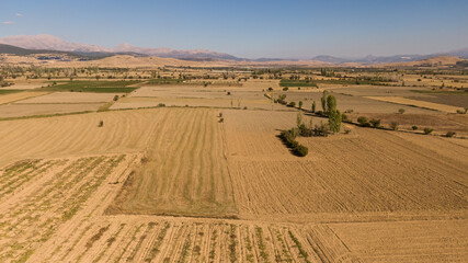 Drone aerial footage of fields lined up in front of a mountain landscape, either harvested or ready for planting. Agriculture, rural life, and land.