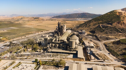 Aerial drone footage of a massive cement or industrial plant located in a mountainous and rural area. Industry, environment, production.