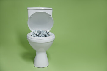 Dollar banknotes in toilet bowl on green background. Space for text