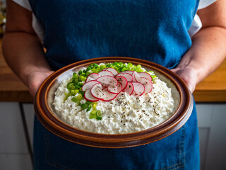 Woman holding plate with cottage cheese with scallions and radishes, close-up
