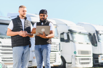 Logistics managers planning routes using laptop near trucks