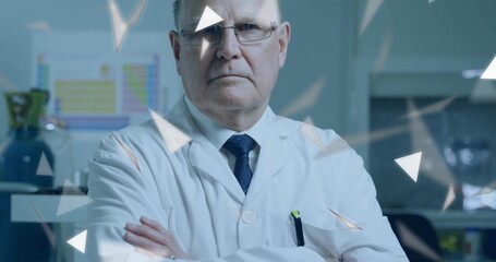 Senior scientist wearing lab coat crossing arms in lab with periodic table and gas cylinder