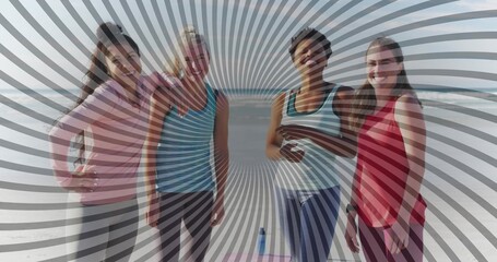 Smiling friends wearing athletic tops and leggings at oceanfront beach, with yoga mat, water bottle