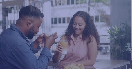 Friends in pink blouse and blue shirt sharing coffee at cafe table by window, with croissants
