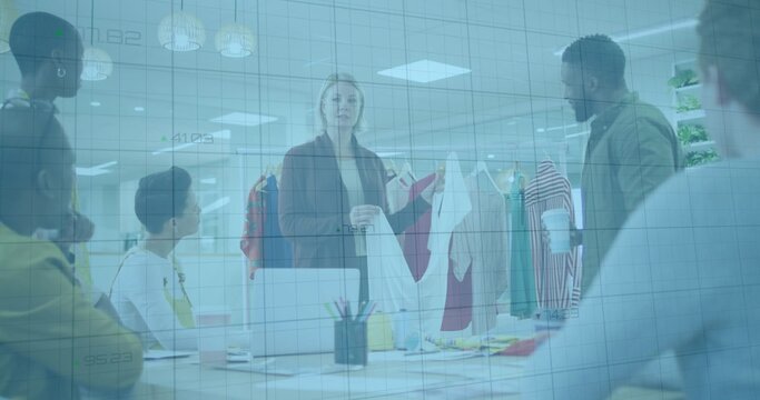 Presenting woman wearing blazer holding white blouse in office meeting, with laptops swatches rack