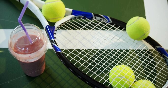 Lying blue tennis racket on ping pong table with yellow tennis balls and purple-straw smoothie cup