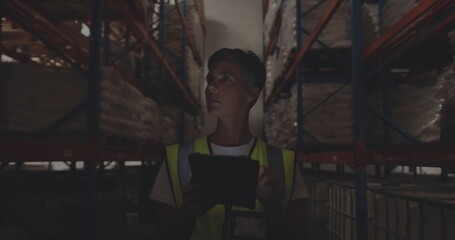 Scanning metal shelving racks, worker wearing safety vest with badge using tablet in narrow aisle