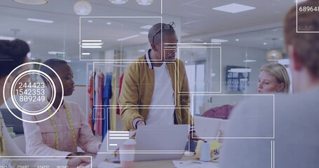 Leading man in mustard jacket guiding team in design studio, with laptops coffee cups tape swatches