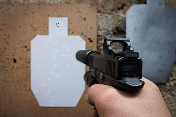 First-person view of tactical shooting practice, aiming a modern handgun with a suppressor and red dot sight at a target.