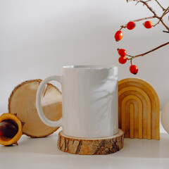 Mockup white mug with autumn decor, rose hips branches and aesthetic shadows. Tea or coffee mug with copy space for autumn design, gift, thanksgiving holiday, halloween