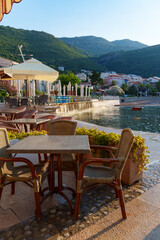 cozy outdoor cafe or restaurant located on embankment with panoramic view of Petrovac city, Montenegro, tables and chairs in front of sea and beach