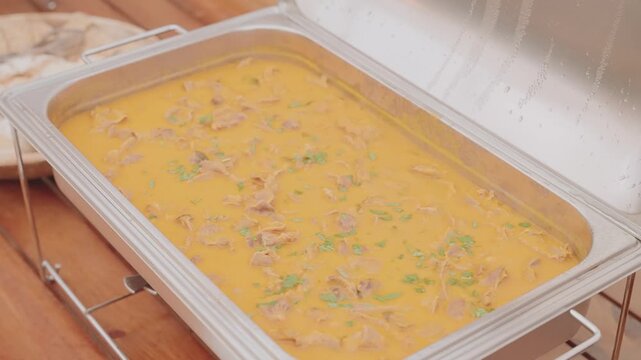 Close up of Portuguese bifanas in rich sauce on stainless buffet tray