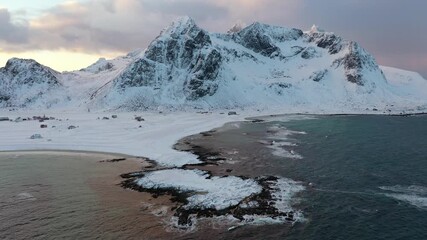 Aerial view of snow-dusted mountains meeting the tranquil sea, creating an evocative contrast of textures and tones, Ramberg, Nordland, Norway.