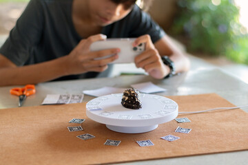 A young man concentrates on taking sequential photographs of a natural sea shell on a rotating 3D scanning platform. 