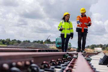 Two engineers wearing safety helmets and high-visibility jackets inspecting a railway track at a...