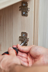 Repairman assembling cabinet and screwing door hinge at home, close-up