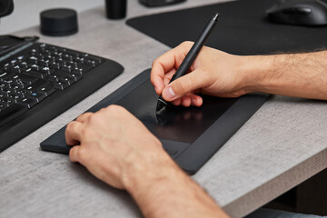 male hands drawing and retouching image on pc computer, using graphic digital tablet and stylus pen at office desk.