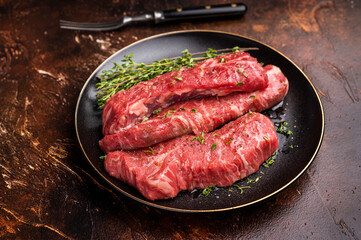 Tri tip steaks, Raw marbled beef meat on plate with herbs. brown background. top view