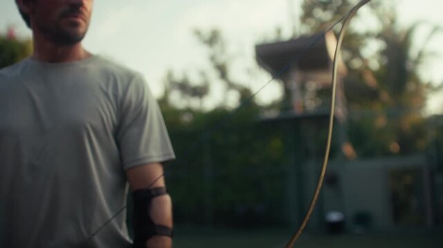 A focused young adult male demonstrates skill in archery, drawing back a traditional bow with an arrow, aiming for accuracy. His precise movements highlight the concentration required for the sport.