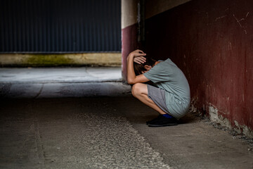 Scared fearful small boy covering face. Boy shouts covered his face with his hands, bullying. A lonely boy sits in tunnel. Sad child suffering from depression sitting alone in alley loneliness