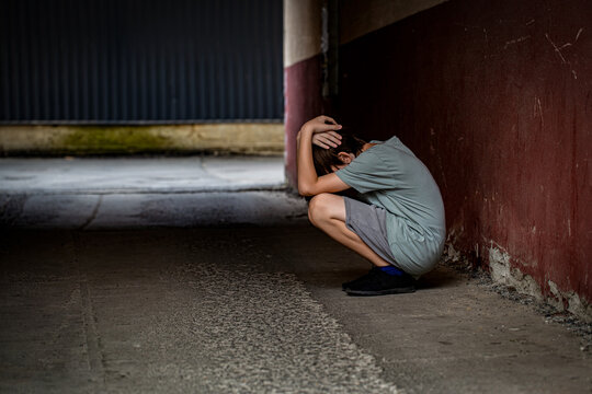 Scared fearful small boy covering face. Boy shouts covered his face with his hands, bullying. A lonely boy sits in tunnel. Sad child suffering from depression sitting alone in alley loneliness