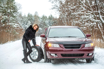 Female using changing wheel. Woman changing the punctured tyre on his car in winter. Pretty girl replacing tyres. Fault car in the winter. Girl trying to repair the car, engine repair, tire change