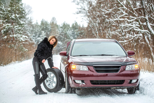 Female using changing wheel. Woman changing the punctured tyre on his car in winter. Pretty girl replacing tyres. Fault car in the winter. Girl trying to repair the car, engine repair, tire change