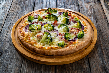 Pizza with bacon, broccoli and red onion on wooden table