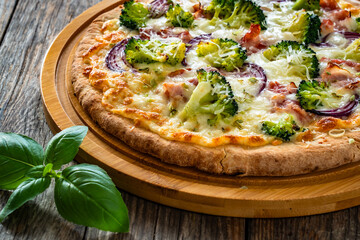 Pizza with bacon, broccoli and red onion on wooden table