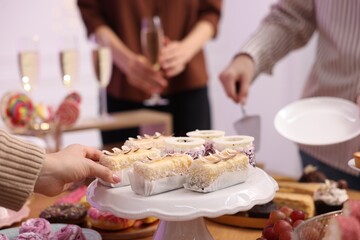 People taking different desserts from buffet table, closeup