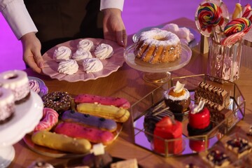 Waiter arranging delicious desserts on buffet table, closeup