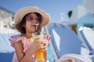 Funny cute girl drinks a cocktail on summer vacation. The child has fun on the beach. Cute baby in a colorful swimsuit and sunglasses is resting.