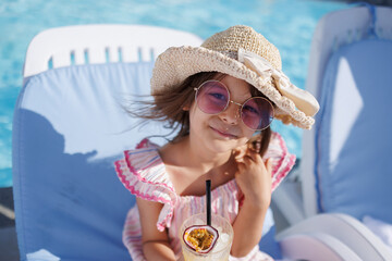 Funny cute girl drinks a cocktail on summer vacation. The child has fun on the beach. Cute baby in a colorful swimsuit and sunglasses is resting.