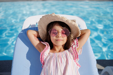 Funny little girl relaxing on summer vacation. The child has fun on the beach. Cute baby in a colorful swimsuit and sunglasses is resting.