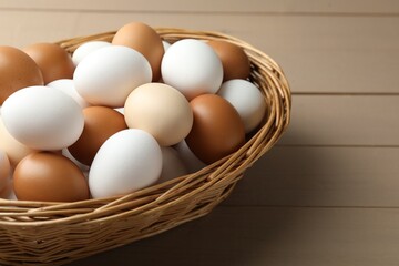 Many raw chicken eggs in wicker basket on wooden table, closeup
