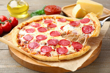 Taking piece of delicious pepperoni pizza at wooden table, closeup