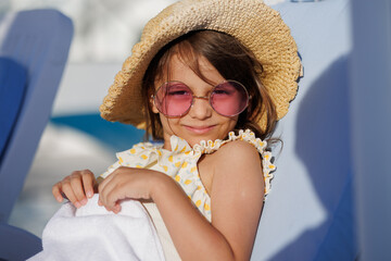 Funny little girl relaxing on summer vacation. The child has fun on the beach. Cute baby in a colorful swimsuit and sunglasses is resting.