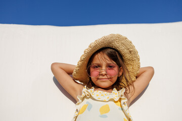 Funny little girl relaxing on summer vacation. The child has fun on the beach. Cute baby in a colorful swimsuit and sunglasses is resting.