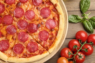 Delicious pepperoni pizza, fresh tomatoes and basil on wooden table, flat lay