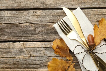 Beautiful table setting. Cutlery with napkin and autumn decor on wooden background, top view. Space for text