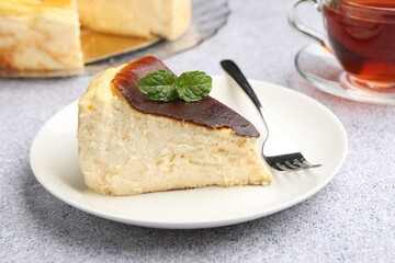 Piece of delicious Basque cheesecake with mint and tea on light grey table, closeup