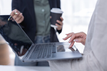 Business women are collaborating, discussing, and working together, analyzing data on a laptop computer, demonstrating teamwork and dedication in a modern office setup with coffee
