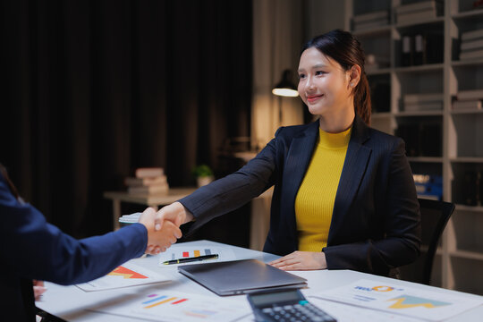 Young Asian businesswomen shaking hands after closing a successful deal or partnership agreement, symbolizing collaboration, trust, and mutual respect in a professional office setting