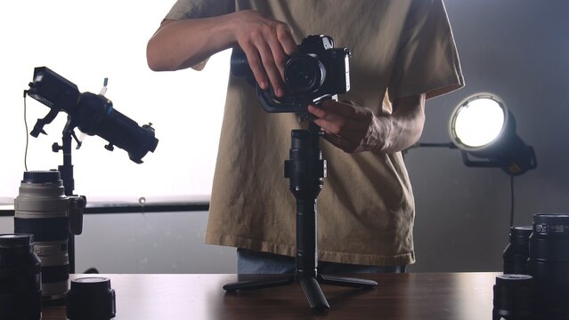 A photographer is adjusting a camera mounted on a stabilizer, with various lenses and studio lights visible.