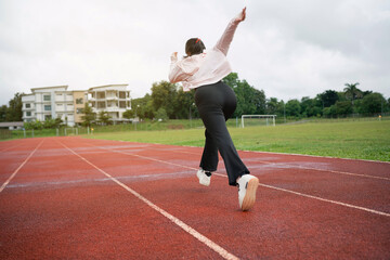 Young woman wearing formal attire running on a track field, showcasing determination and energy in an athletic environment, dramatic sky in the background