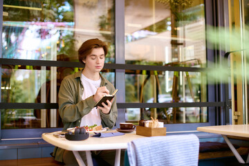 Young man dining and writing in a cozy, modern cafe