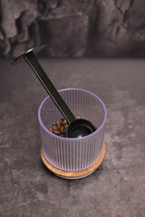 Dark roasted coffee beans in a transparent glass with a black spoon inside on a wooden board. Dark background. Still Life. Place for adding text, design