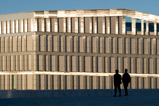 Two people walking beside building facade during golden hour showing human presence interaction and movement in Oslo contemporary business district