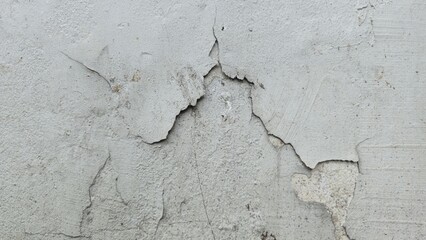 Gray cement wall surface with cracks and peeling paint revealing inner layers, showing rough...
