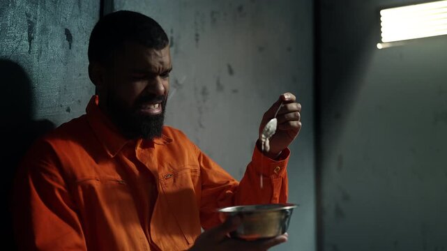 Unhappy African American inmate eating bland prison food, punishment life